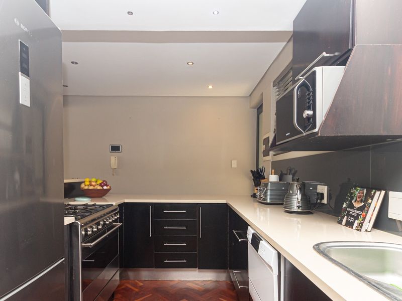 Modern kitchen featuring dark cabinetry, quartz countertops, gas stove, integrated appliances, and parquet flooring with recessed lighting.