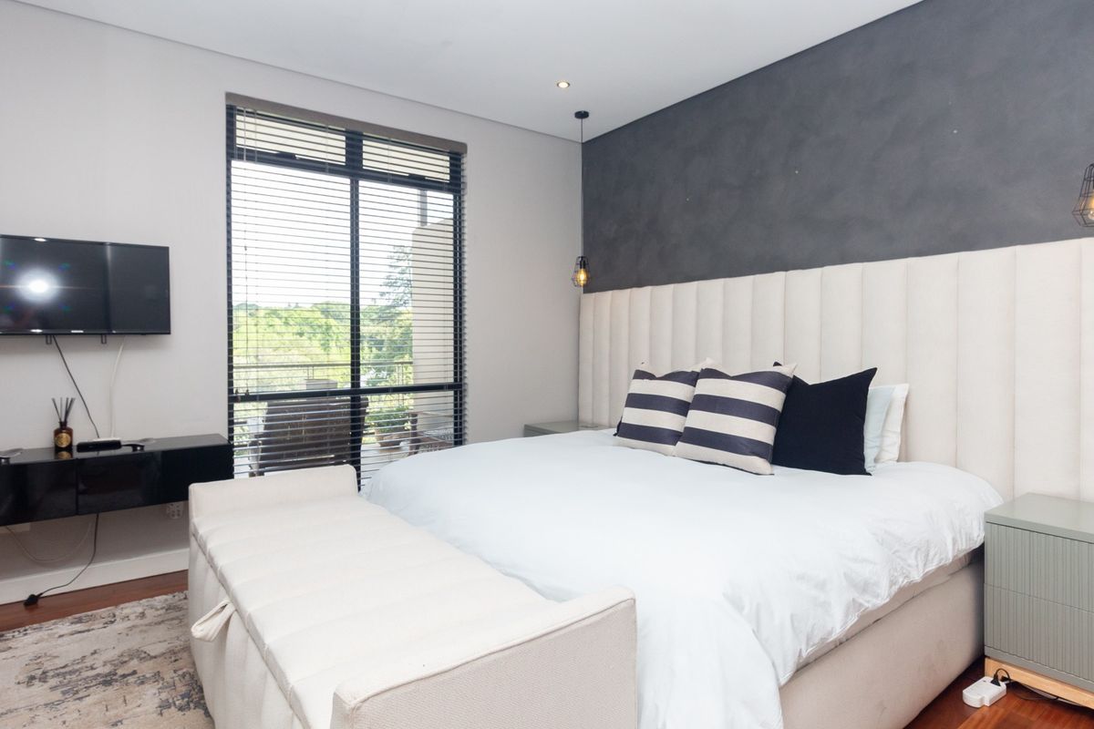 Modern bedroom featuring a dark feature wall, neutral upholstered headboard, recessed lighting, and large window with venetian blinds.