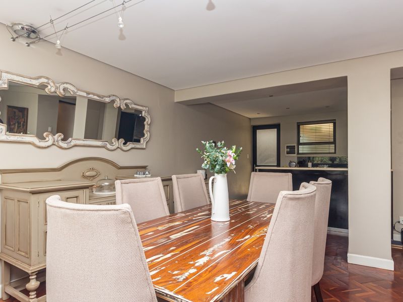 A well-maintained dining room featuring classic parquet flooring and track lighting, with an open-plan layout connecting to the adjacent kitchen area.