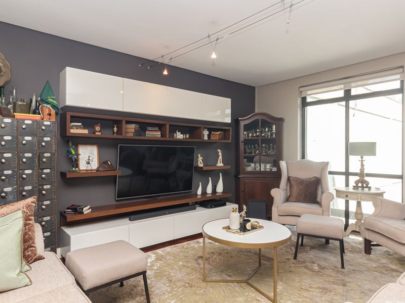 A well-maintained living room featuring built-in media cabinetry, track lighting, and large windows providing natural light.