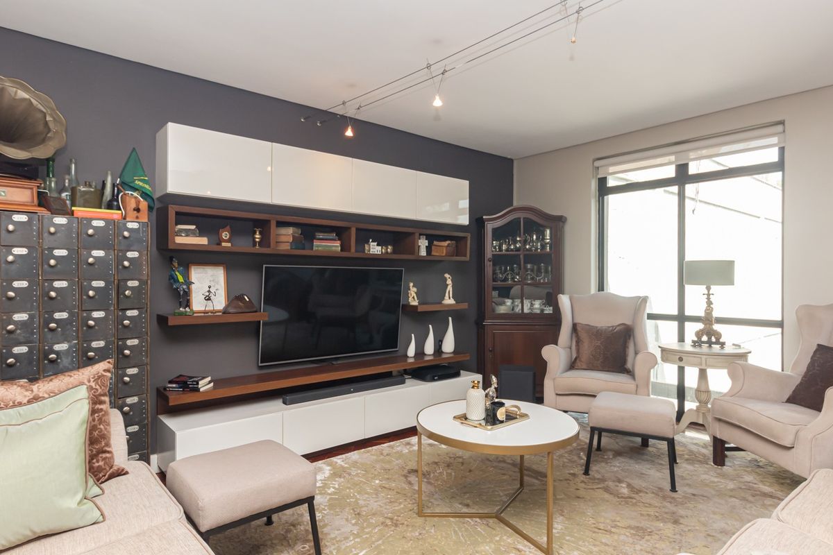 A well-maintained living room featuring built-in media cabinetry, track lighting, and large windows providing natural light.