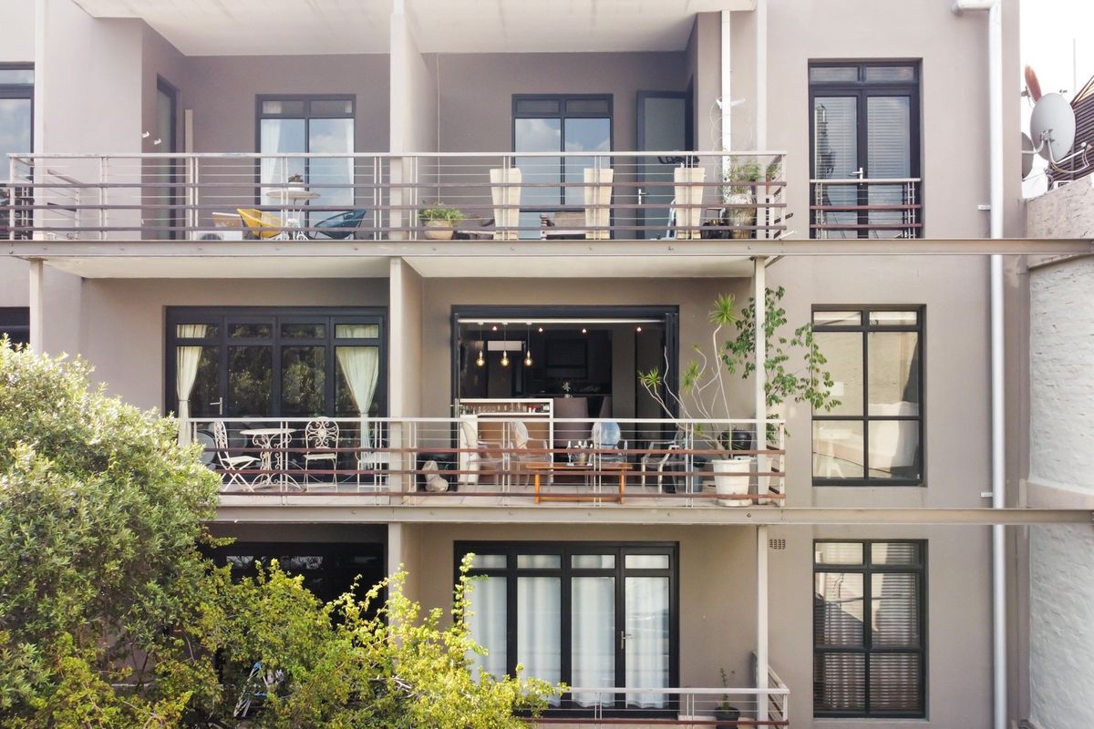 Rear elevation of a multi-story apartment building featuring stacked balconies with metal railings and large sliding glass doors providing access to living spaces.