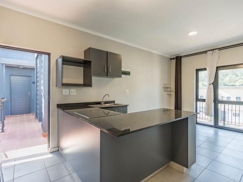 Open-plan kitchen area featuring modern dark cabinetry, granite countertops, and tiled flooring, with direct access to an outdoor balcony space.