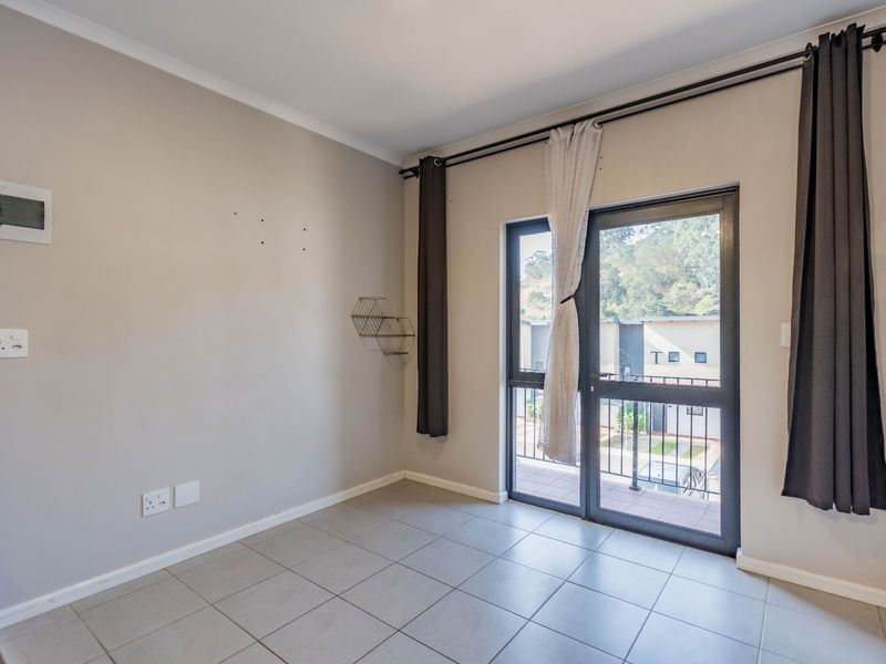 An empty bedroom featuring neutral tiled flooring, a sliding glass door leading to a balcony, and wall-mounted electrical fixtures.