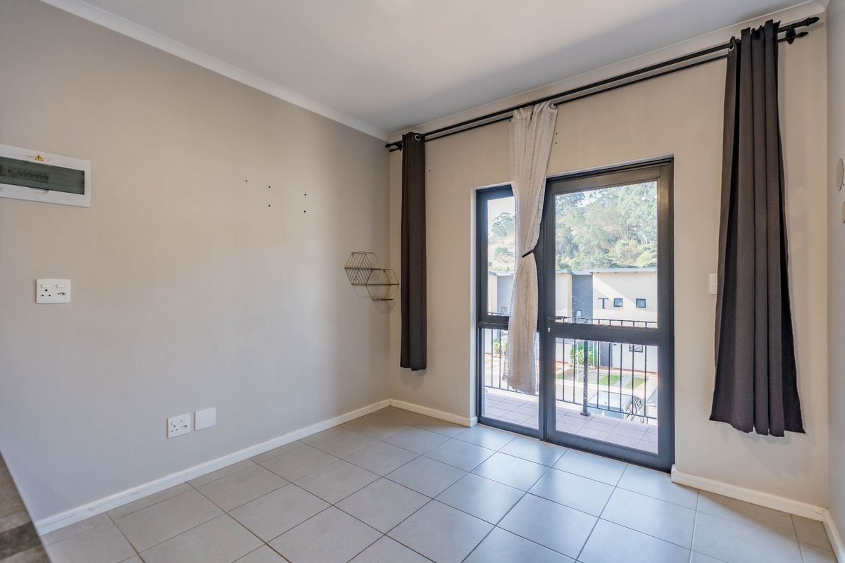 An empty bedroom featuring neutral tiled flooring, a sliding glass door leading to a balcony, and wall-mounted electrical fixtures.