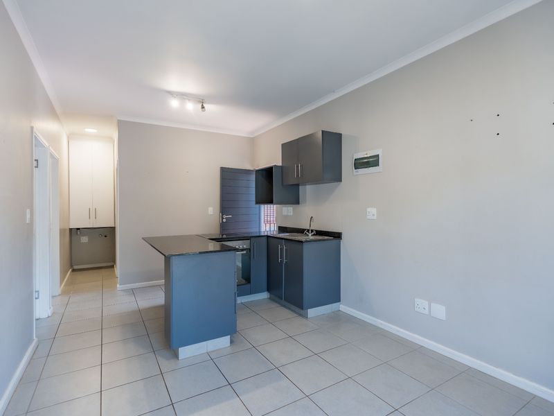 A compact, empty kitchen featuring dark grey cabinetry, granite countertops, built-in oven and hob, and neutral tiled flooring.