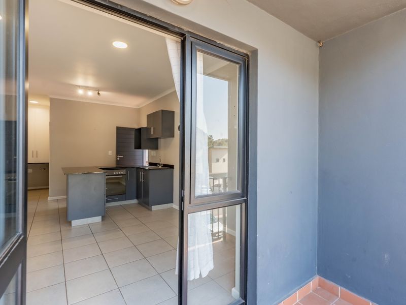 A view from a covered balcony looking into an open-plan kitchen area featuring modern dark cabinetry and tiled flooring.