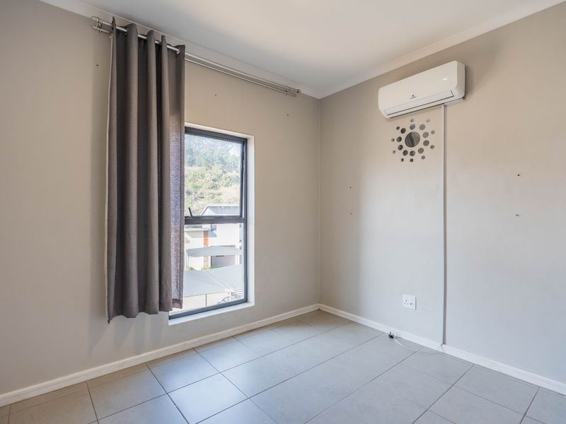 A clean, empty bedroom featuring tiled flooring, a wall-mounted air conditioning unit, and a window with neutral grey curtains.