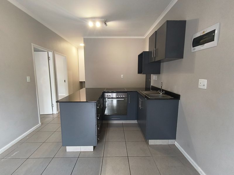 A modern, compact kitchen featuring dark grey cabinetry, granite countertops, a built-in oven and hob, and neutral tiled flooring.
