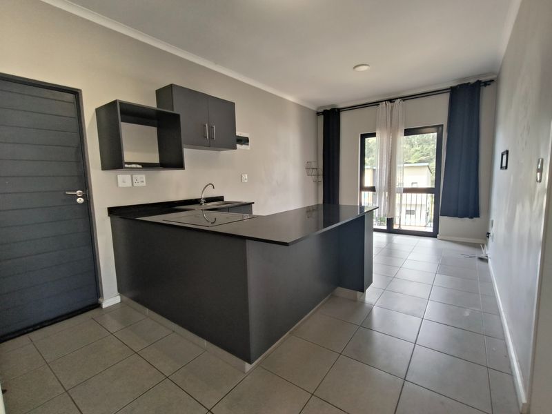 Modern open-plan kitchen and living area featuring dark cabinetry, granite countertops, tiled floors, and direct access to a balcony through sliding glass doors.