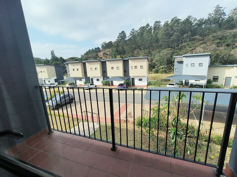A private balcony with tiled flooring and a metal balustrade, offering an elevated view of the apartment complex and surrounding landscape.