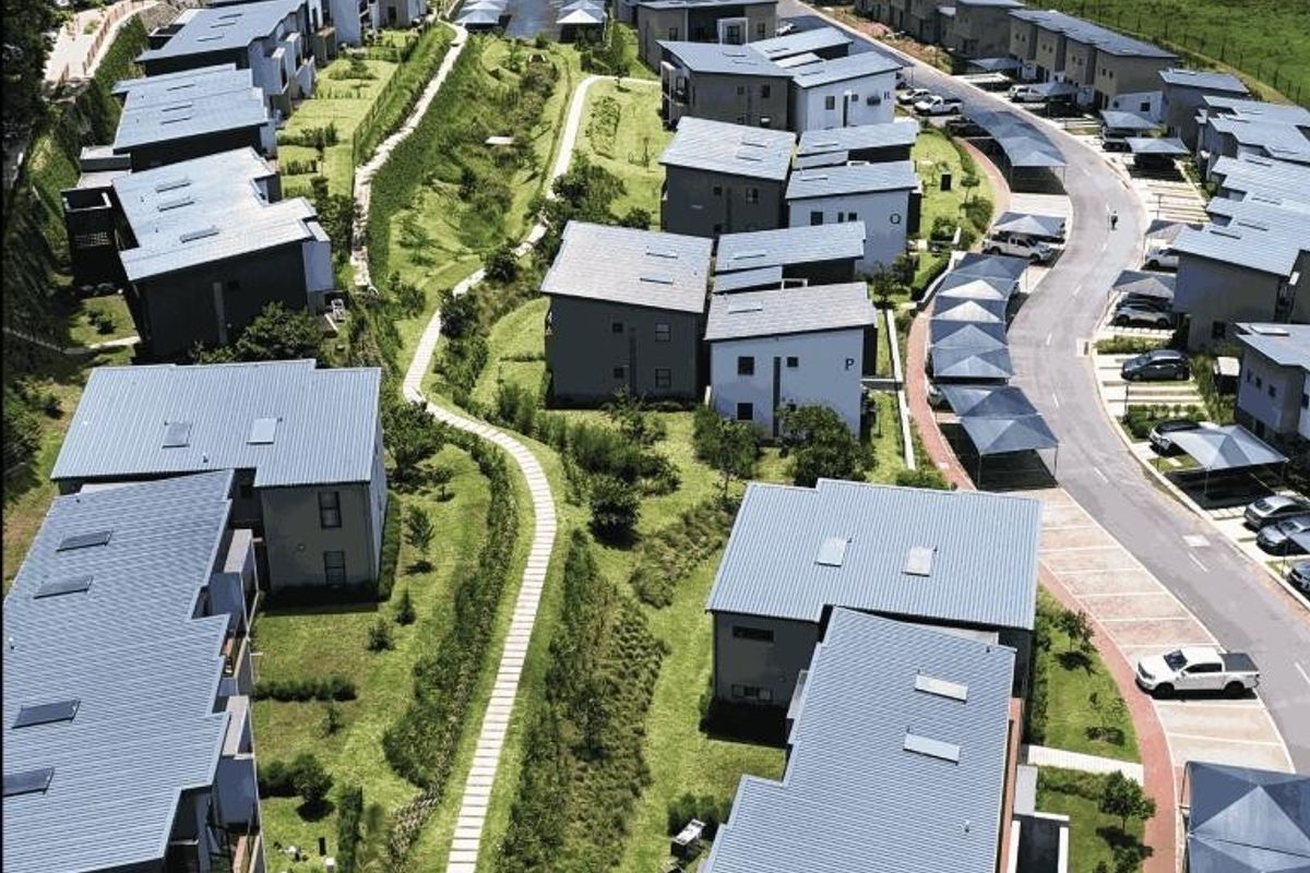An aerial view of a modern residential apartment complex featuring multiple buildings with metal roofs, paved pathways, and covered parking areas.