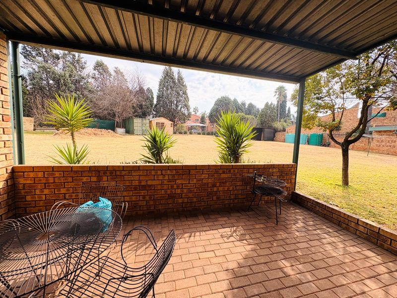 A covered outdoor patio featuring brick walling and paved flooring, overlooking a spacious backyard garden area.