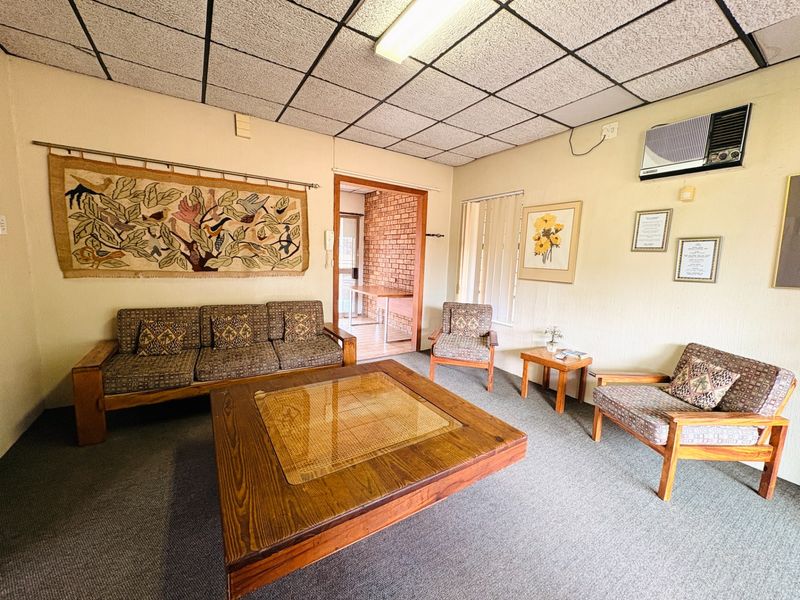 A dated living room featuring a drop ceiling, carpeted flooring, and a wall-mounted air conditioning unit.