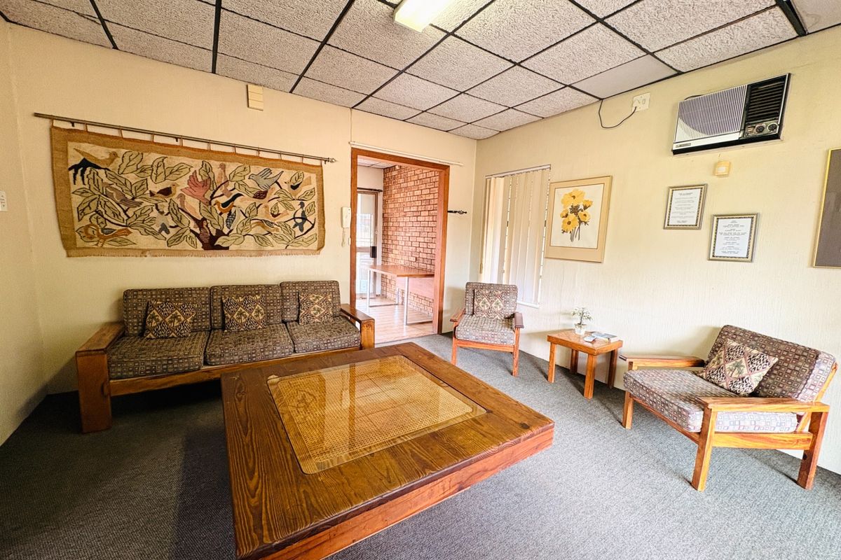 A dated living room featuring a drop ceiling, carpeted flooring, and a wall-mounted air conditioning unit.