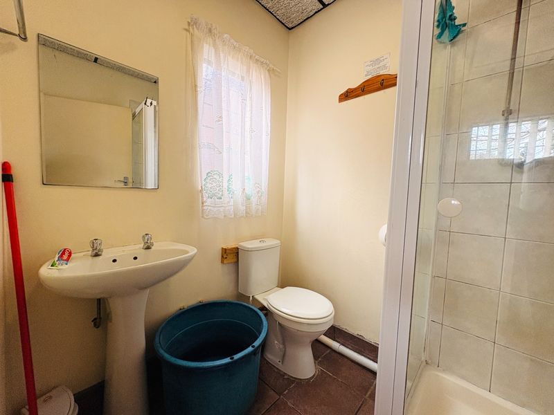 A functional bathroom featuring a pedestal basin, toilet, and shower enclosure with tiled flooring and visible plumbing fixtures.
