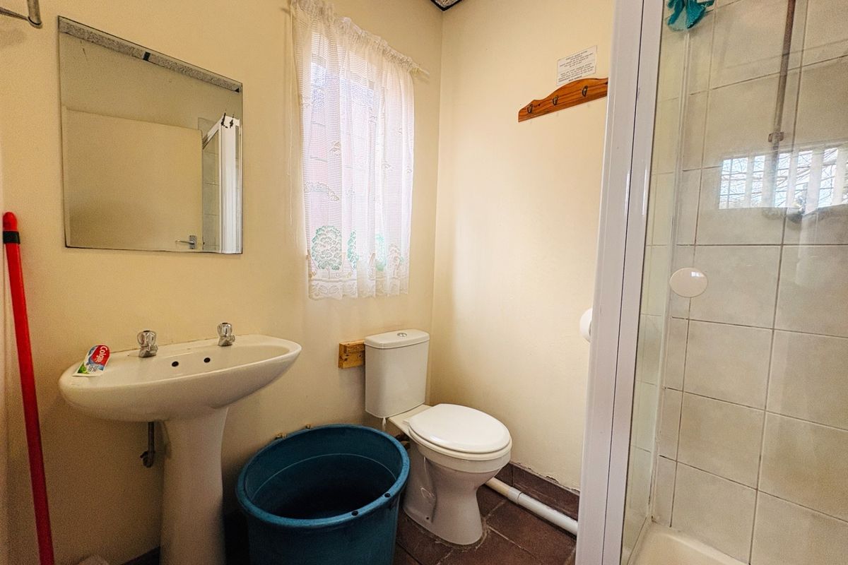 A functional bathroom featuring a pedestal basin, toilet, and shower enclosure with tiled flooring and visible plumbing fixtures.