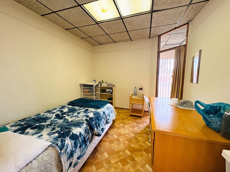 A bedroom featuring dated drop ceiling tiles, fluorescent lighting, and tiled flooring, with direct access to an outdoor area through a glass door.