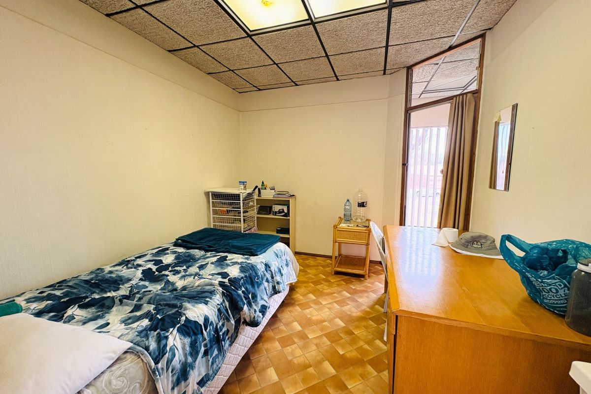 A bedroom featuring dated drop ceiling tiles, fluorescent lighting, and tiled flooring, with direct access to an outdoor area through a glass door.