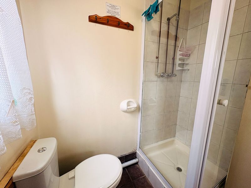 A compact bathroom featuring a shower enclosure with tiled walls and a standard toilet, requiring cosmetic updates to modernize the space.