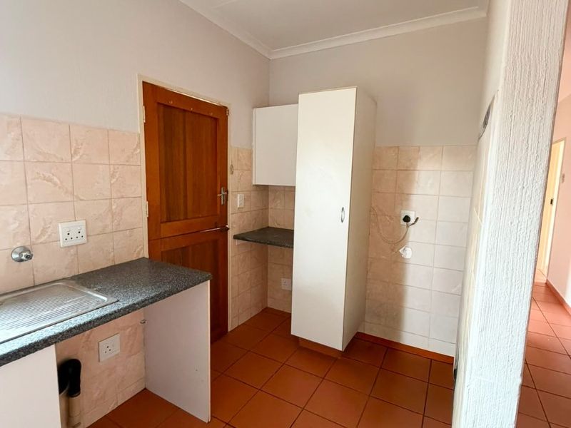 A functional laundry area featuring built-in cabinetry, a stainless steel sink, granite countertops, and durable ceramic floor tiles.