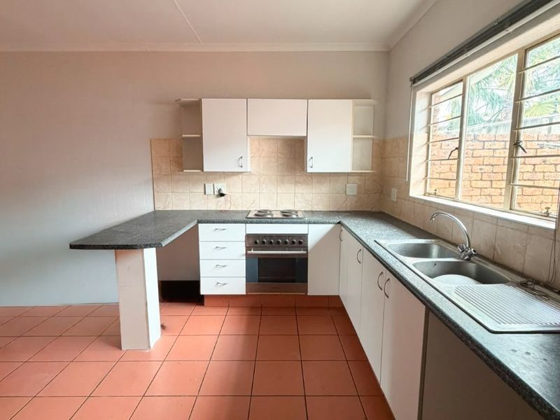 A functional, empty kitchen featuring white cabinetry, dark laminate countertops, a built-in oven with hob, and terracotta-style ceramic floor tiles.
