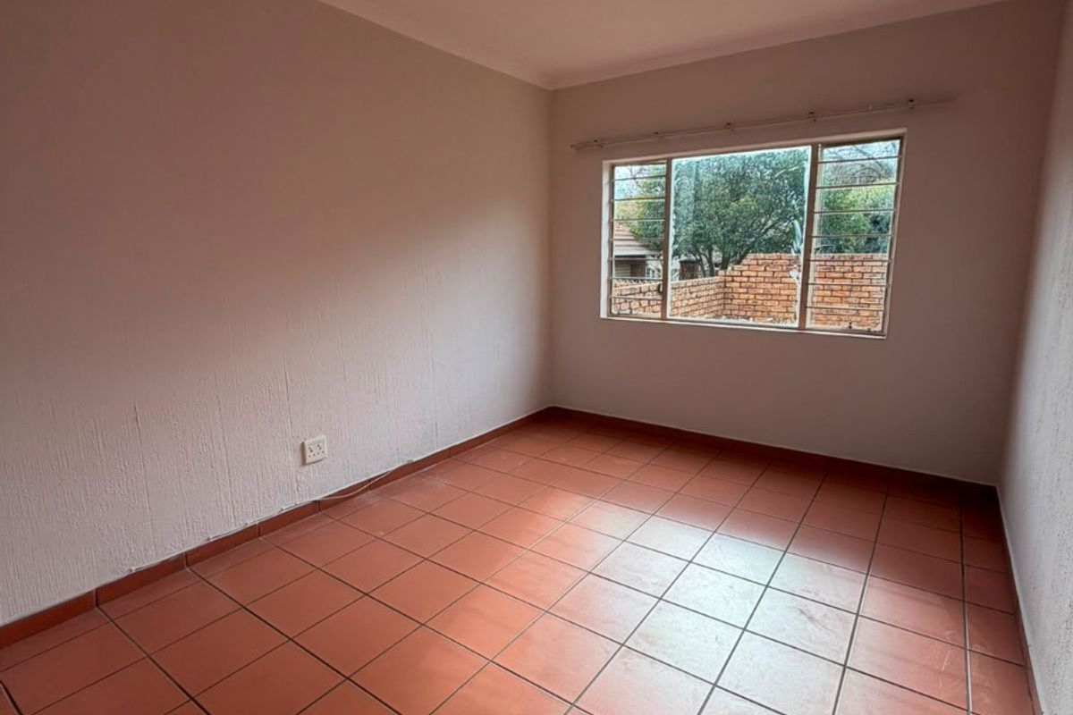 An empty bedroom featuring terracotta-style floor tiles, a steel-framed window, and neutral wall finishes, providing a blank canvas for interior design.