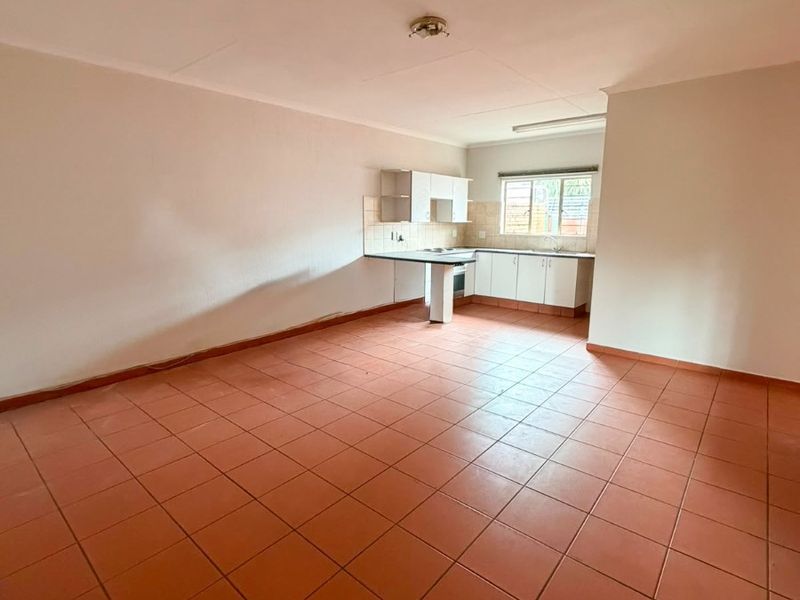 An open-plan living and kitchen area featuring terracotta-style floor tiles, neutral walls, and a functional kitchen layout with built-in cabinetry and a breakfast counter.