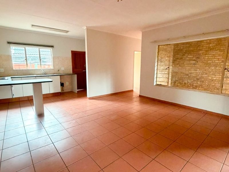 Spacious open-plan living and kitchen area featuring terracotta-style floor tiles, a functional kitchen layout, and a distinctive exposed brick feature wall.