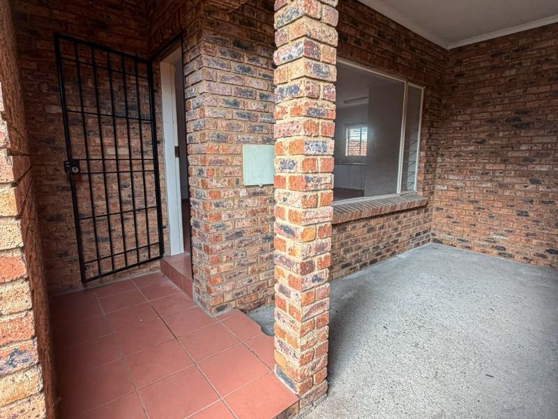 Covered entrance porch featuring face brick construction, a security gate, and tiled step leading to the front door.