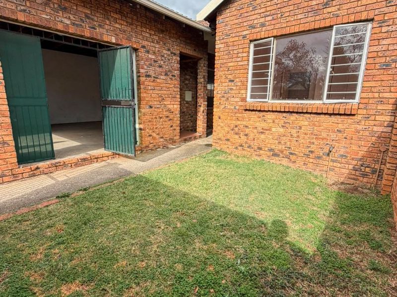 Rear exterior view of a face brick townhouse featuring a small lawn area, concrete pathway, and access to a garage.
