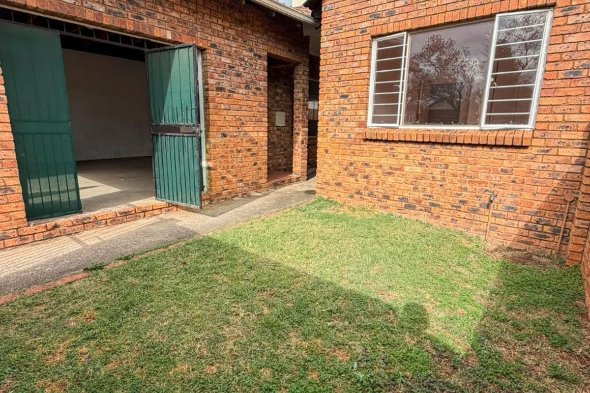 Rear exterior view of a face brick townhouse featuring a small lawn area, concrete pathway, and access to a garage.