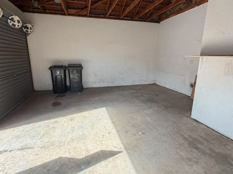 A spacious, functional garage featuring exposed timber roof trusses, concrete flooring, and a secure roller door, offering ample storage or vehicle parking space.