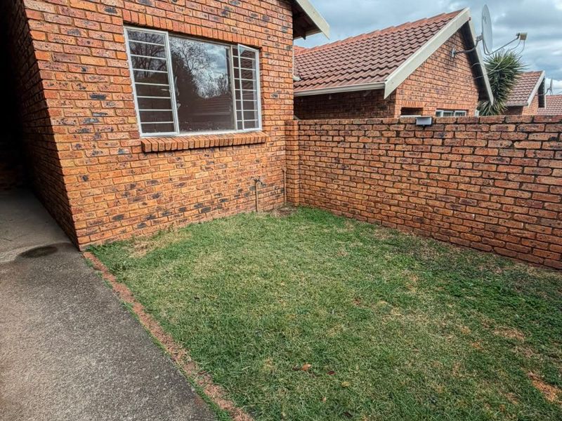 A private rear garden area featuring a face brick exterior, concrete pathway, and enclosed boundary wall, providing a low-maintenance outdoor space.