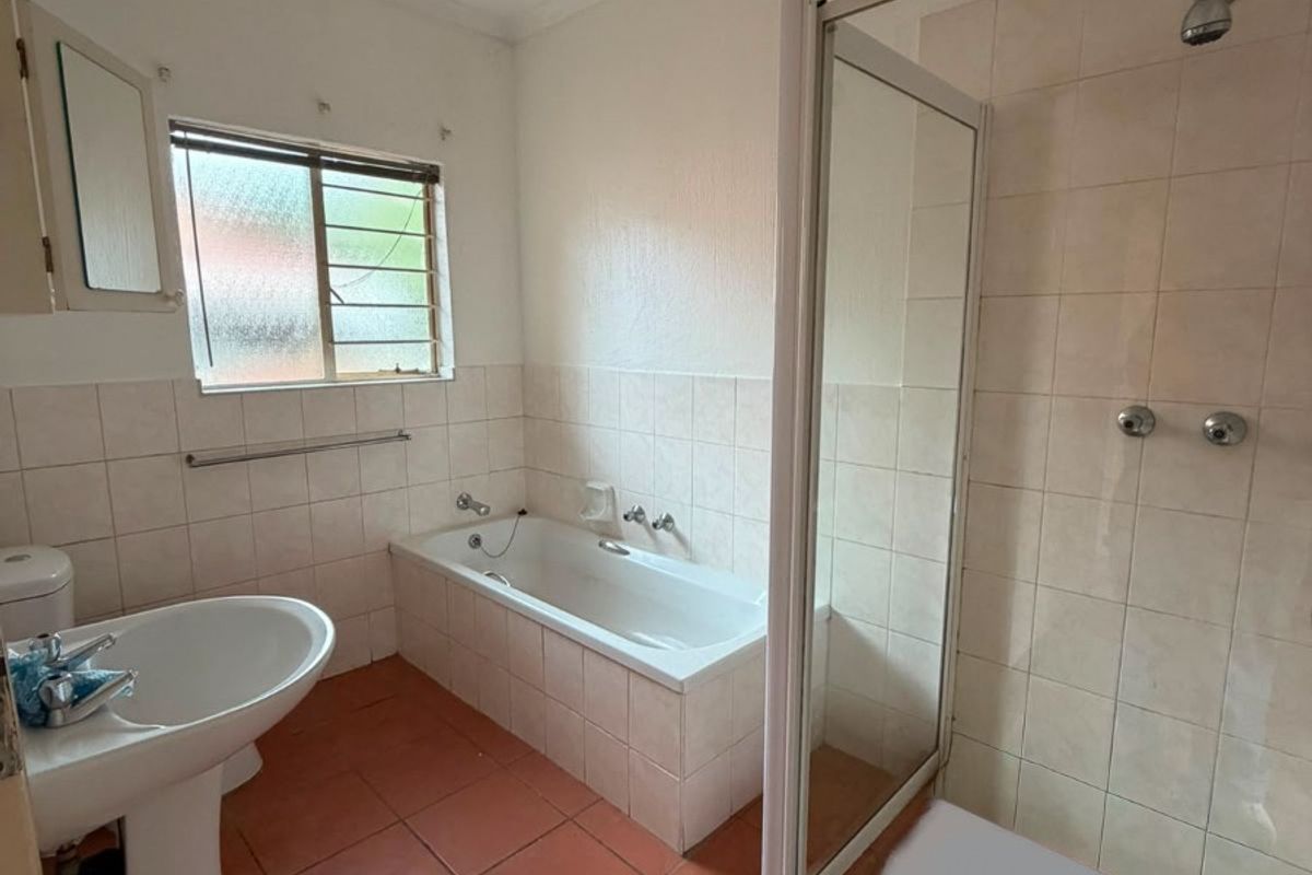 A functional bathroom featuring a pedestal basin, a built-in bathtub, and a separate shower enclosure with tiled finishes throughout.