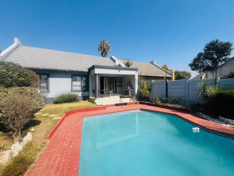 Rear exterior view featuring a swimming pool with brick coping, a covered patio area, and a precast concrete boundary wall.