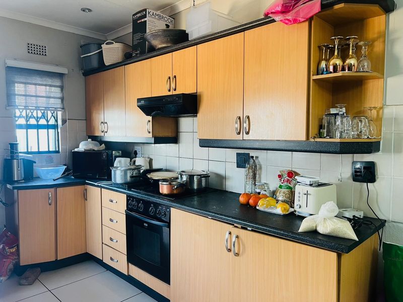 A functional kitchen featuring light wood-tone cabinetry, dark countertops, built-in oven with extractor fan, and tiled backsplash, offering a practical layout for daily use.