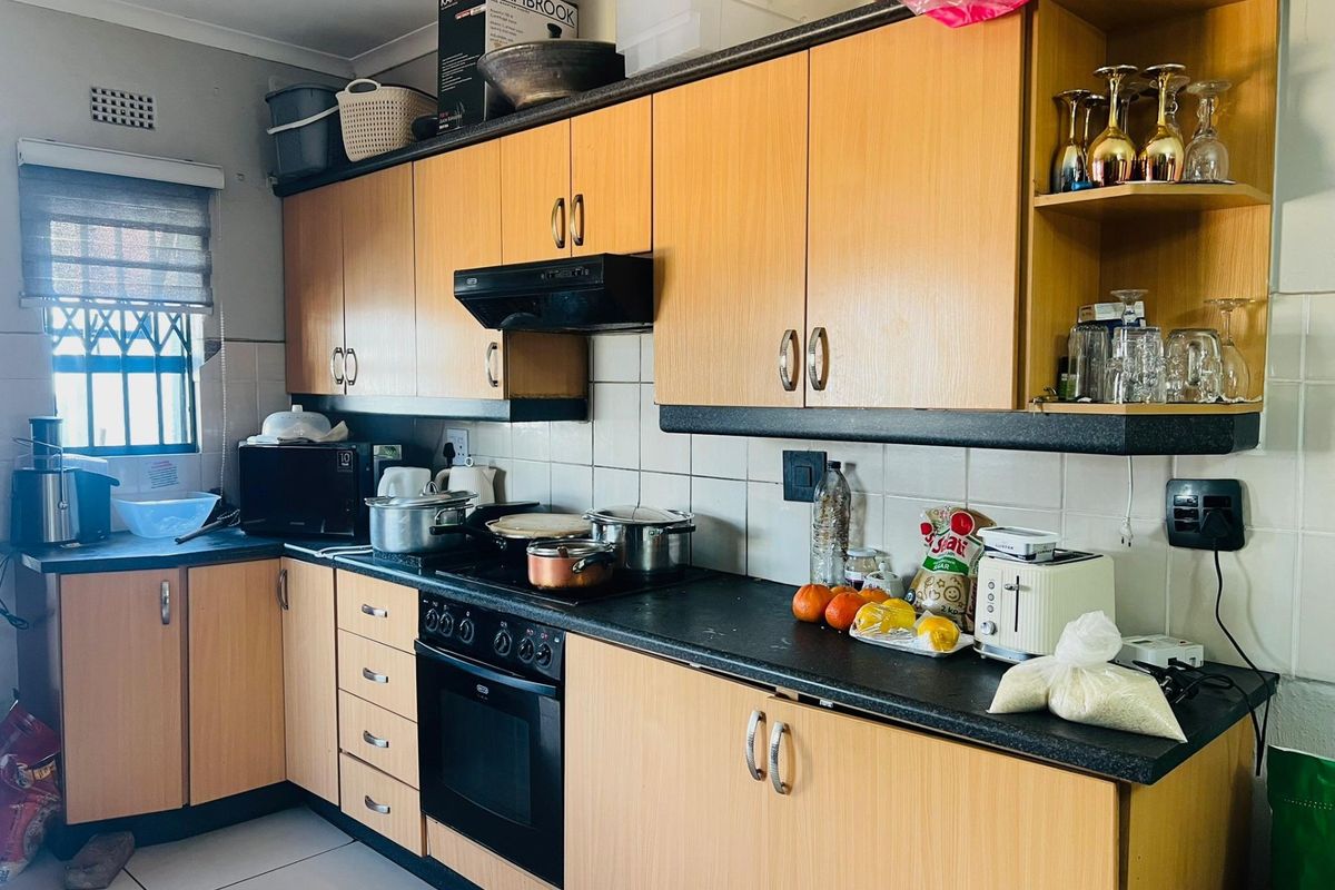 A functional kitchen featuring light wood-tone cabinetry, dark countertops, built-in oven with extractor fan, and tiled backsplash, offering a practical layout for daily use.