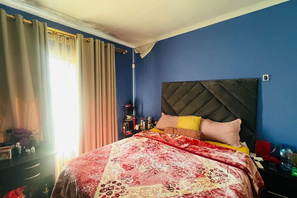 A bedroom featuring blue walls and a window with curtains. The ceiling shows signs of damage in the corner.