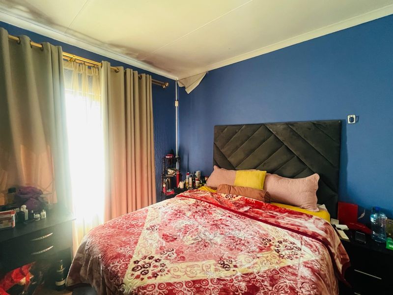 A bedroom featuring blue walls and a window with curtains. The ceiling shows signs of damage in the corner.