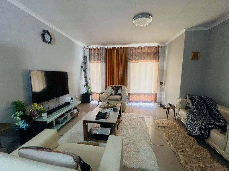 A comfortable living room featuring tiled flooring, coved ceilings, and large windows with curtains, providing a functional and well-lit space for relaxation.