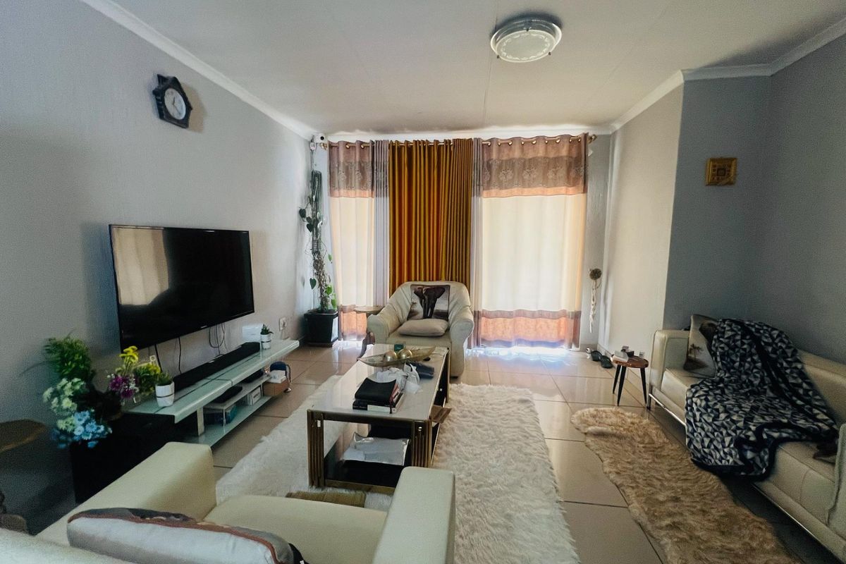 A comfortable living room featuring tiled flooring, coved ceilings, and large windows with curtains, providing a functional and well-lit space for relaxation.