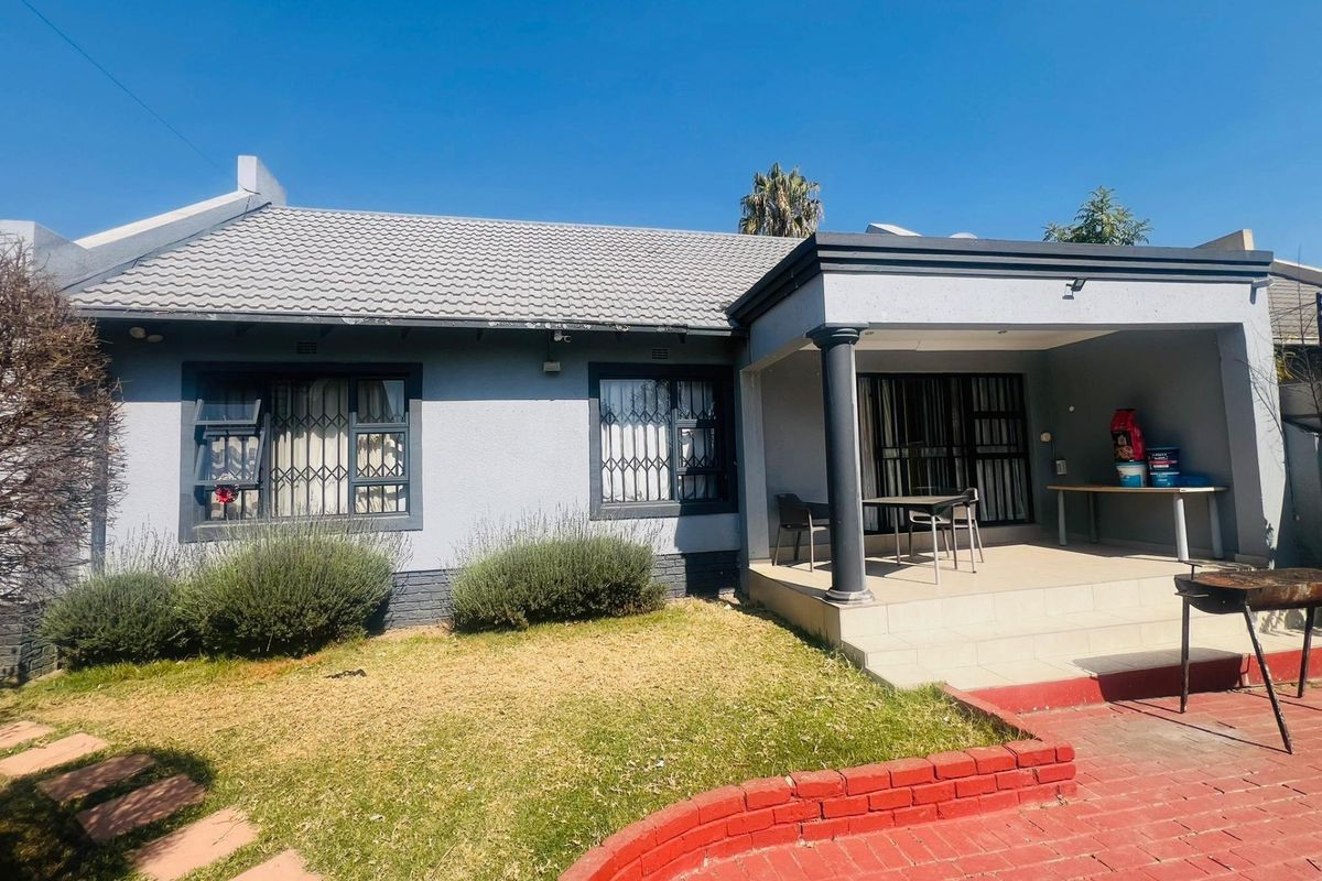 Rear view of the house featuring a covered patio, tiled roof, and a brick-paved area with a small garden.