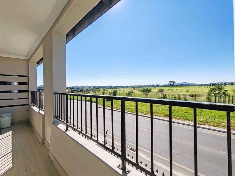 A spacious covered balcony featuring a metal balustrade and tiled flooring, offering an open view of the surrounding landscape and street.