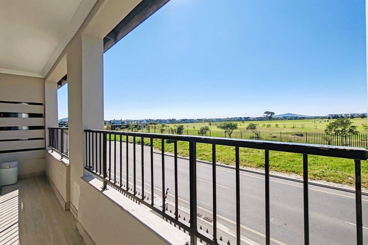 A spacious covered balcony featuring a metal balustrade and tiled flooring, offering an open view of the surrounding landscape and street.