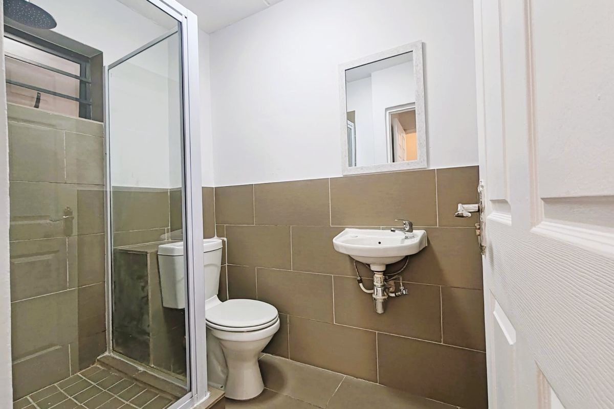 A functional bathroom featuring a glass-enclosed shower, wall-mounted basin, and toilet with neutral-toned wall and floor tiling.