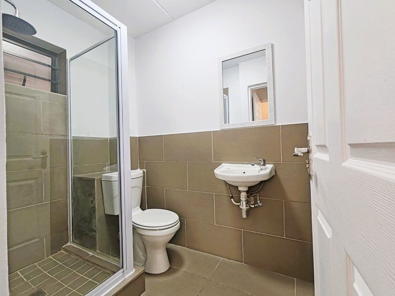 A functional bathroom featuring a glass-enclosed shower, wall-mounted basin, and toilet with neutral-toned wall and floor tiling.