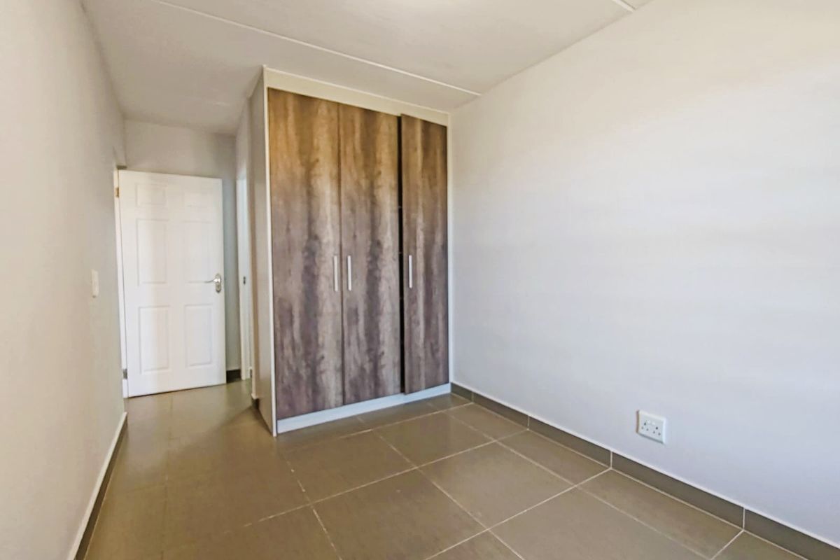 A clean, empty bedroom featuring neutral tiled flooring and a modern wood-finish built-in wardrobe.