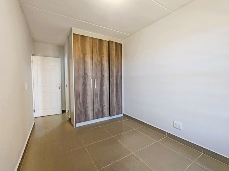 A clean, empty bedroom featuring neutral tiled flooring and a modern wood-finish built-in wardrobe.