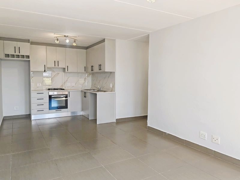 Modern open-plan kitchen featuring light grey cabinetry, marble-look splashback, built-in oven and hob, and neutral tiled flooring throughout the living area.